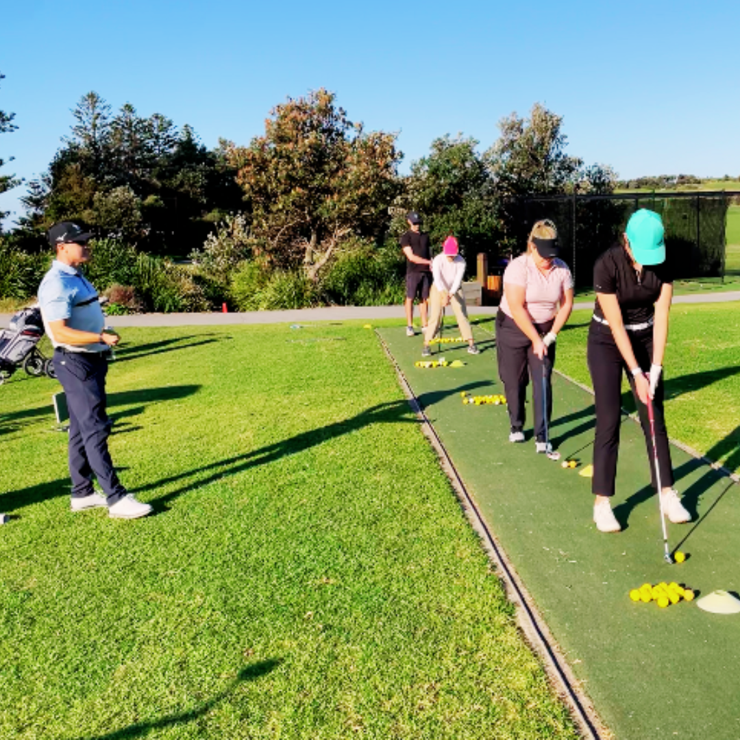 Golf instructor watching beginners practise their swings in a line on the driving range.